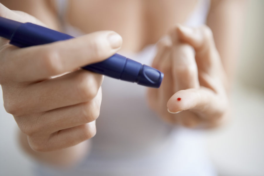 Close das mãos de uma mulher fazendo o exame de diabete. Um dos dedos está com um gota de sangue