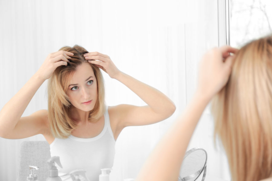 Mulher mexendo no cabelo na frente do espelho vendo se está desenvolvendo calvície feminina