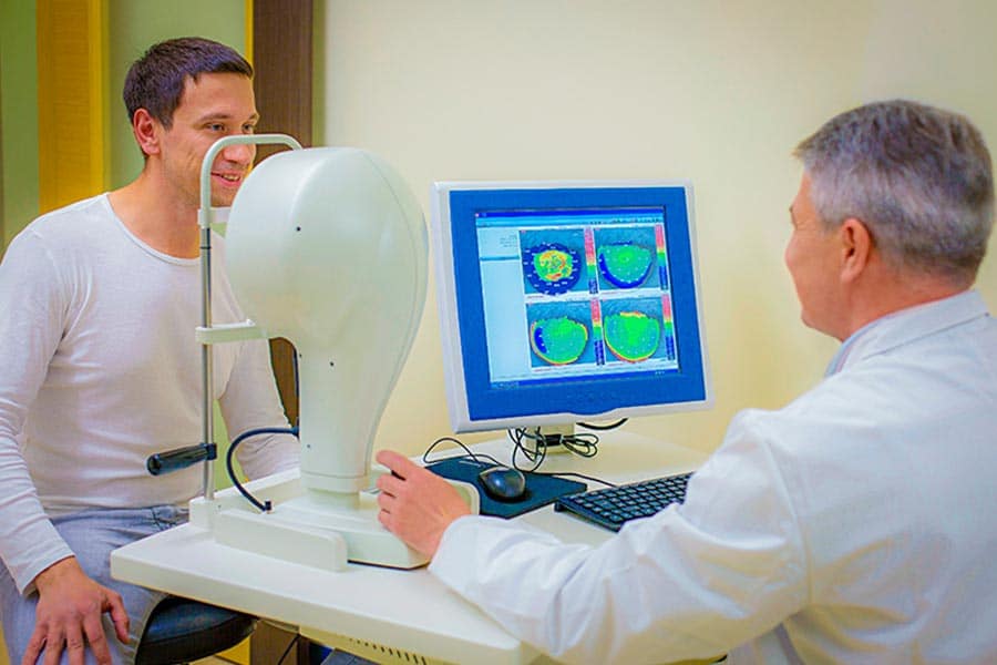 Médico examinando o olho de um paciente por meio de um aparelho que faz parte dos exames oftalmológicos