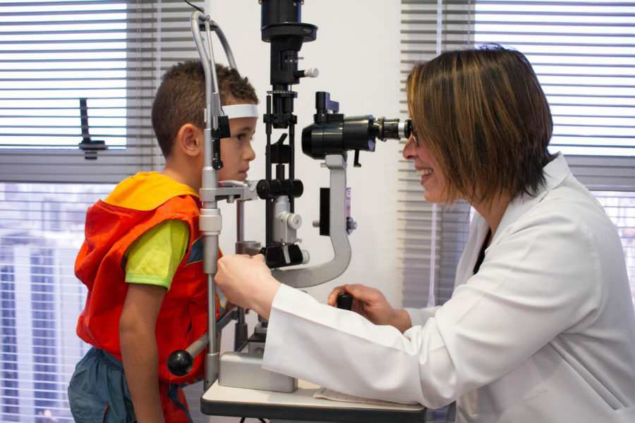 Médica sorridente fazendo um exame na primeira consulta oftalmológica em uma criança.