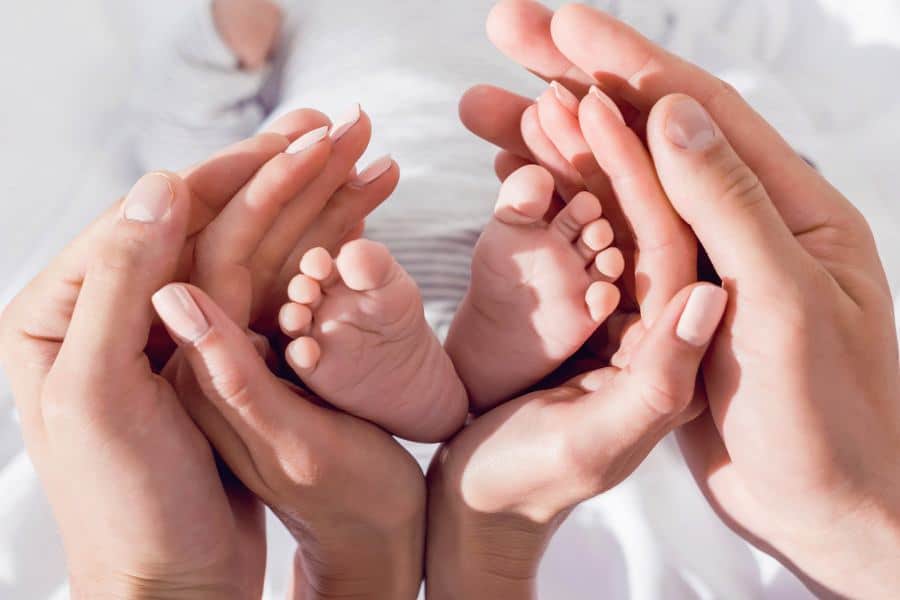 Mãos dos pais envolvem o pé do bebê fazendo o formato de um coração