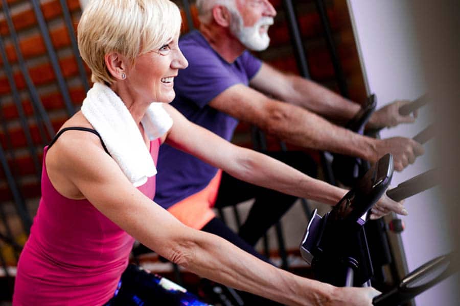 Casal de idosos se exercitando na bicicleta ergométrica, uma das forma de prevenir a osteoporose.