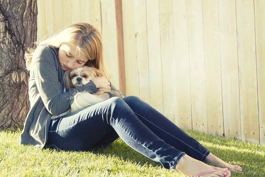 Garota triste sentada na grama abraçando um pequeno cachorro