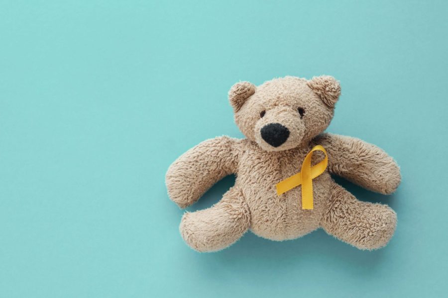 Urso de pelúcia com fita amarela sob um fundo azul piscina representando o o combate ao câncer infantil