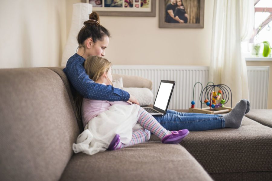 Mãe e filha abraçadas no sofá de casa mexendo no computador representando o uso da tecnologia na infância