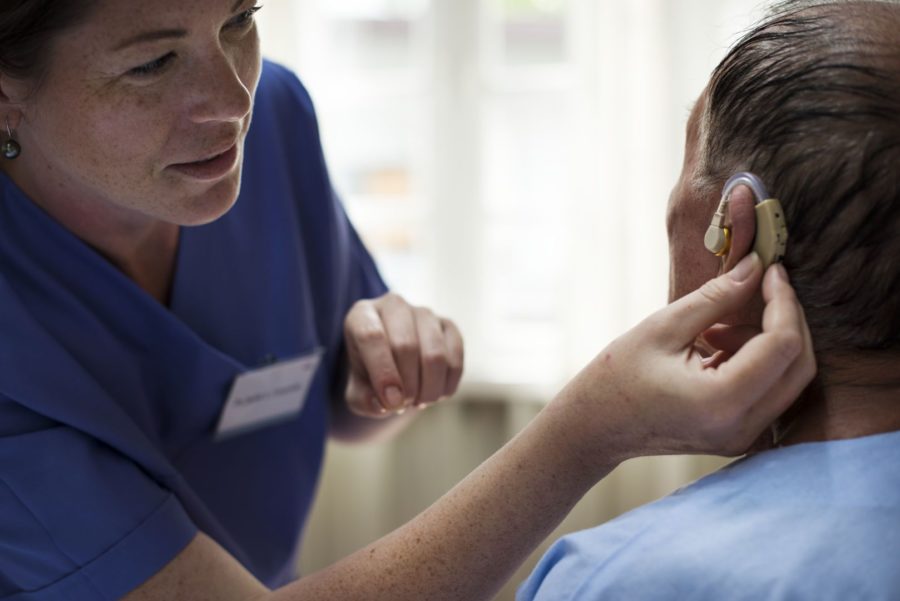 Médica colocando aparelho auditivo em paciente idoso que está com quadro de surdez