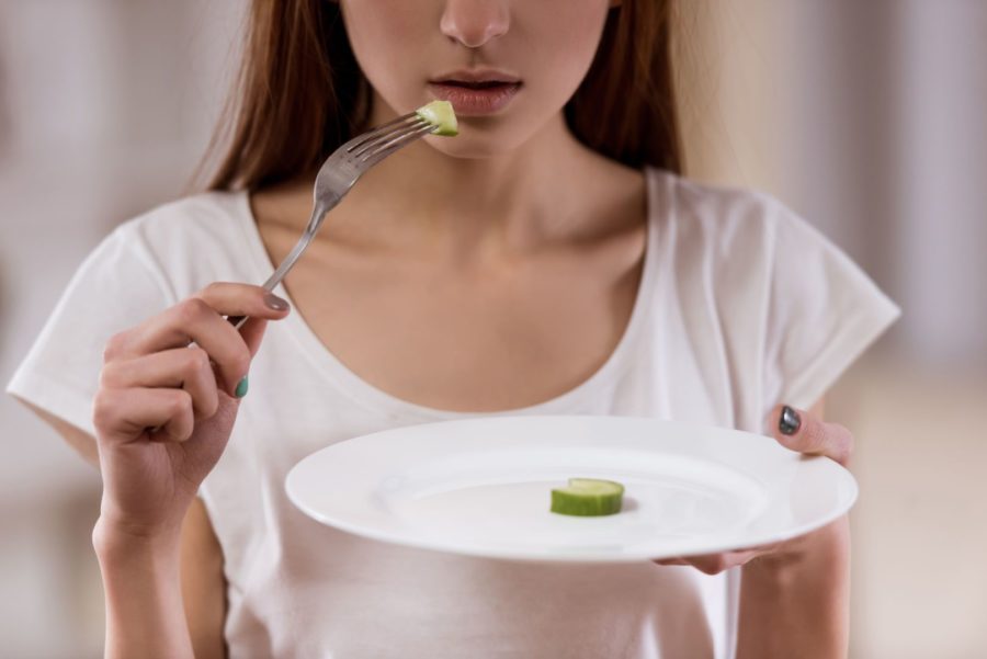 Close de menina segurando um prato que contém apenas um pepino para representar um transtorno alimentar