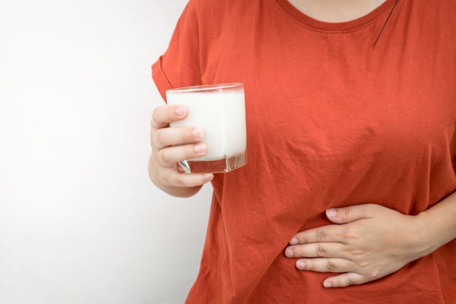Close da barriga de uma jovem com uma das mão apoiando no abdômen indicando dor no estômago decorrente da alergia à proteína do leite de vaca e na outra mão um copo de leite