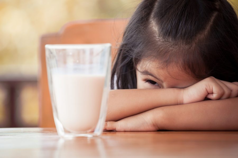 Menina debruçada na mesa com um cara sofrida olhando para um copo de leite