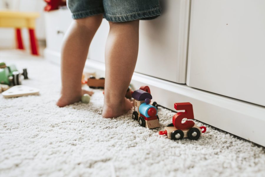 Close de pernas de criança em pé no quarto brincando para representar os problemas ortopédicos na infância. No chão, alguns brinquedos.