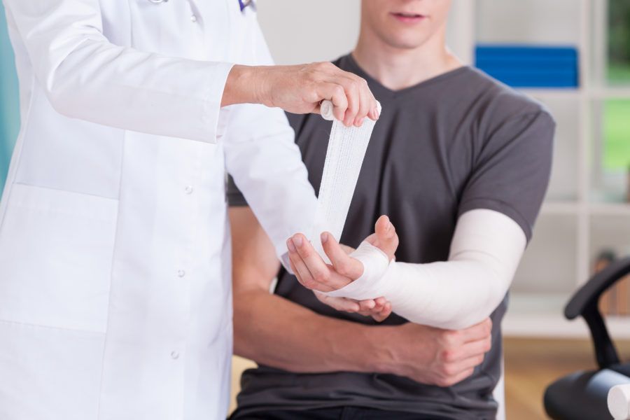 Médica enfaixando braço de um homem devido a fratura do escafóide