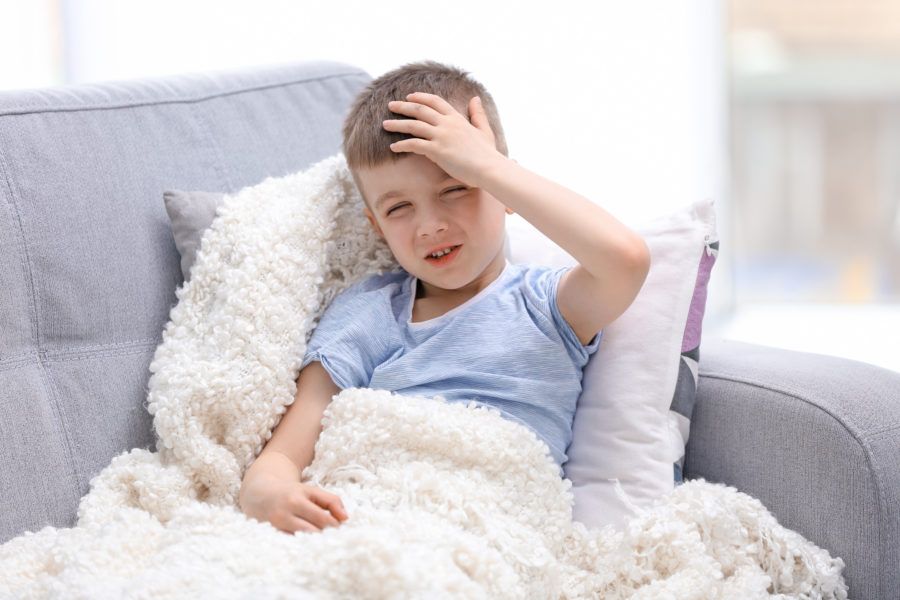 Menino no sofá de casa com dor de cabeça proveniente de meningite