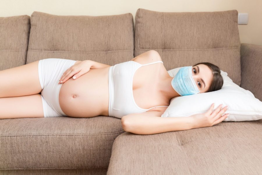 Grávida com coronavírus deitada no sofá usando uma máscara de proteção
