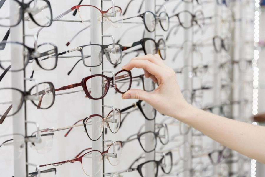 close de mão escolhendo uma armação de óculos dentre várias opções expostas na ótica