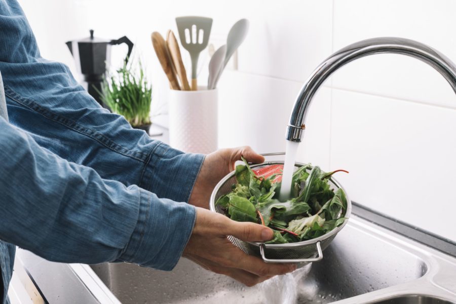 Homem lavando verduras na pia da cozinha para prevenir da toxoplasmose