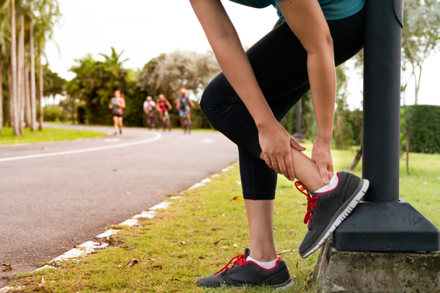 Ao ar livre, mulher corredora segurando o tornozelo da perna por ter sofrido uma fratura por estresse