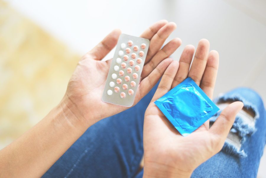 Mulher segurando dois tipos de métodos contraceptivos, uma camisinhas e pílulas