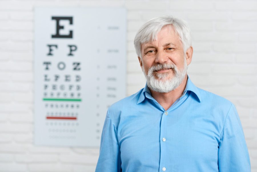Homem idoso em um consultório oftalmológico para saber se é o momento certo de fazer cirurgia de catarata. Ao fundo, Optotipos