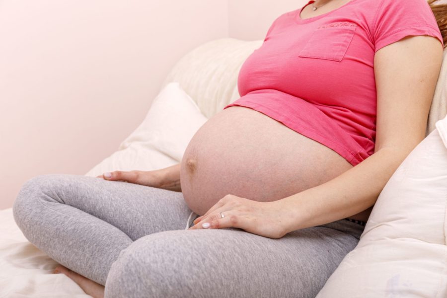 Mulher gravida sentada na cama com as pernas cruzadas