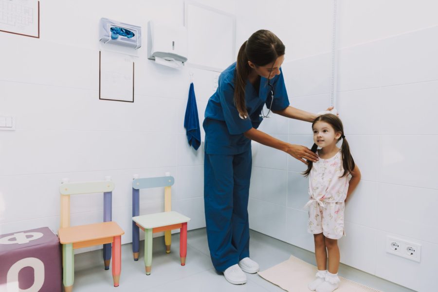 Criança em um consultório médico tendo sua altura media por uma pediatra para poder acompanhar o seu crescimento