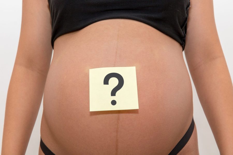 Close da barriga de uma grávida com um post it com um ponto de interrogação indicando as dúvidas sobre a gestação
