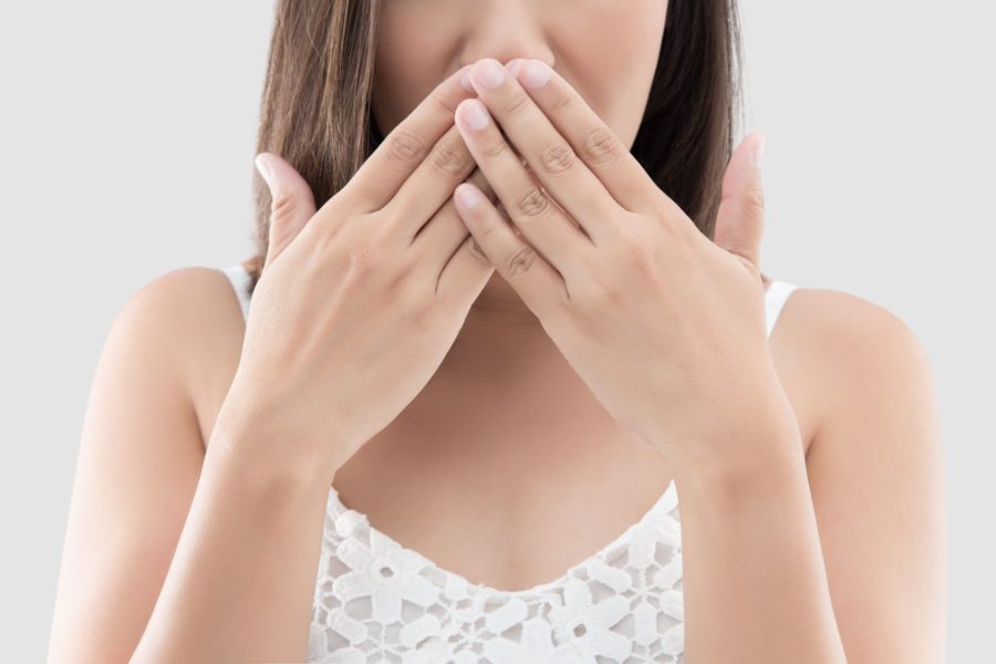 Mulher tampando a boca com as mãos indicando que ela tem mau hálito.