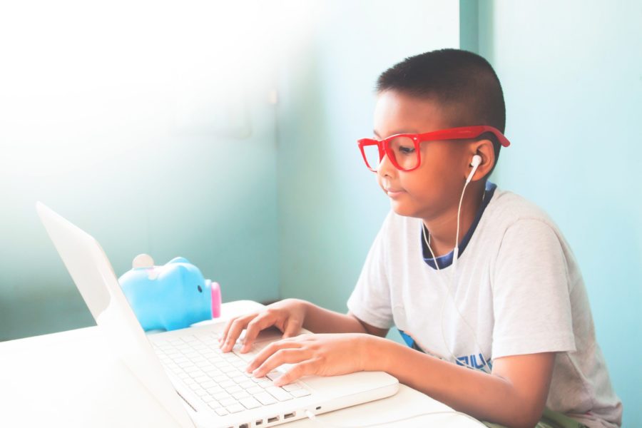 Menino com óculos infantis vermelho usando um notebook branco