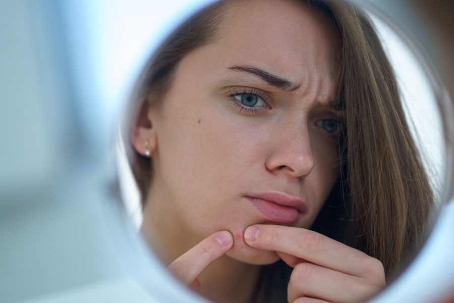 Reflexo no espelho do rosto mulher aparentemente apreensiva apertando uma acne no seu queixo
