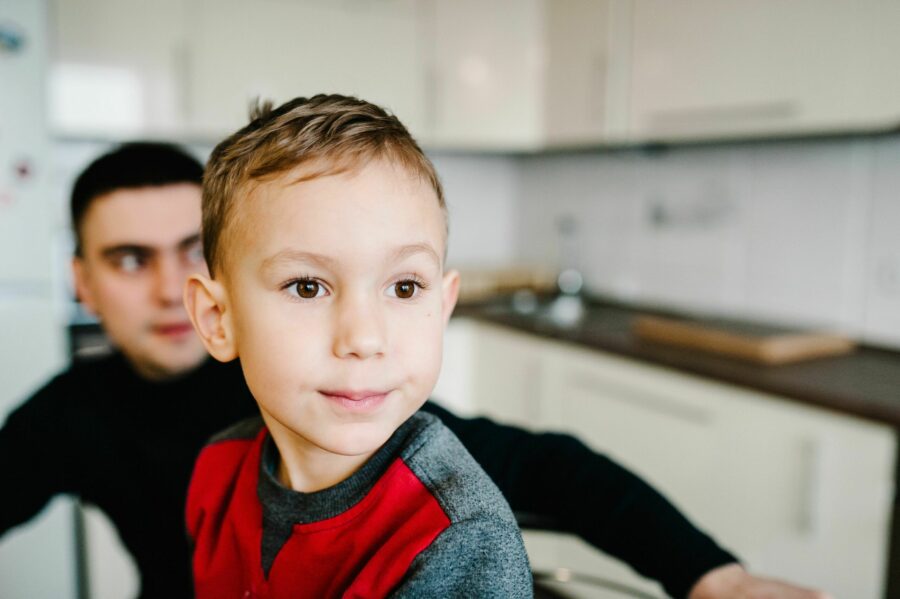 Retrato de criança com autismo em primeiro plano e pai atrás desfocado