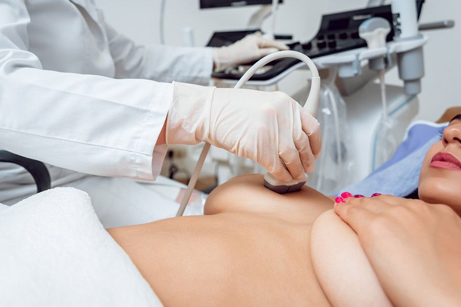 Médica fazendo um procedimento de ultrassom em uma das mamas de uma mulher para ver se ela tem nódulos nas mamas