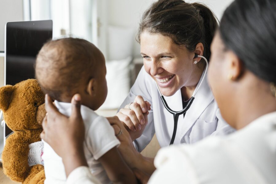 Em um consultória. pediatra mulher está sorrindo para uma criança negra que é segurada pela mãe