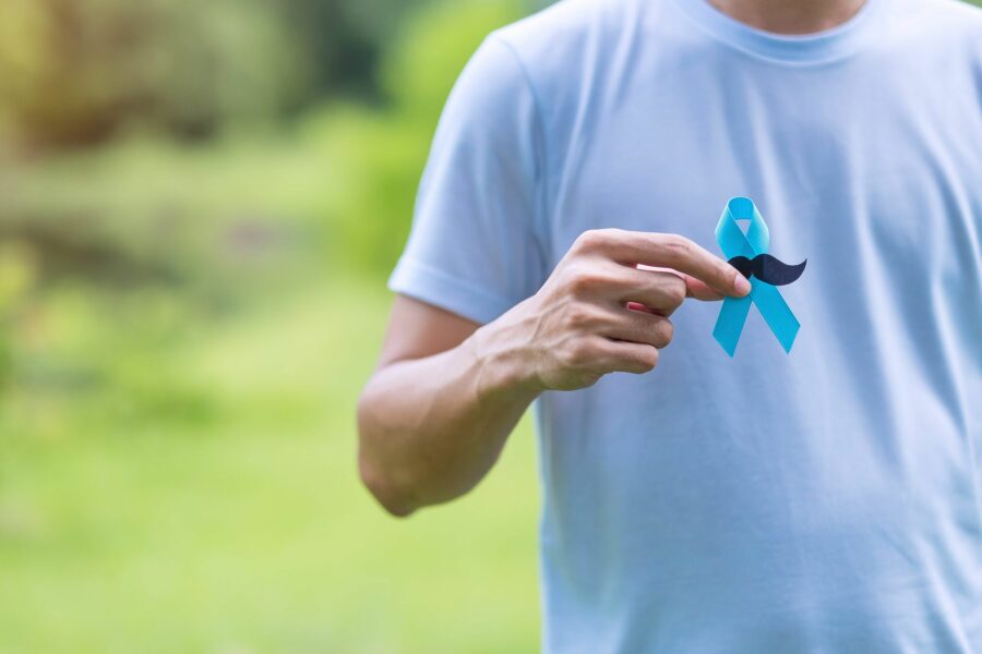 Homem segurando uma fita azul com bigodes para alertar sobre o novembro azul, mês de conscientização sobre o câncer de próstata