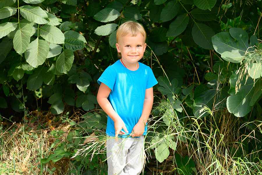 Ao ar livre, garoto sorridente de uns 4 a 7 ano com autismo está mexendo em sua blusa azul.
