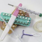 Vários métodos contraceptivos (diu, camisinha, pílula, teste de gravidez, injeção) e um termômetro sobre um fundo branco.